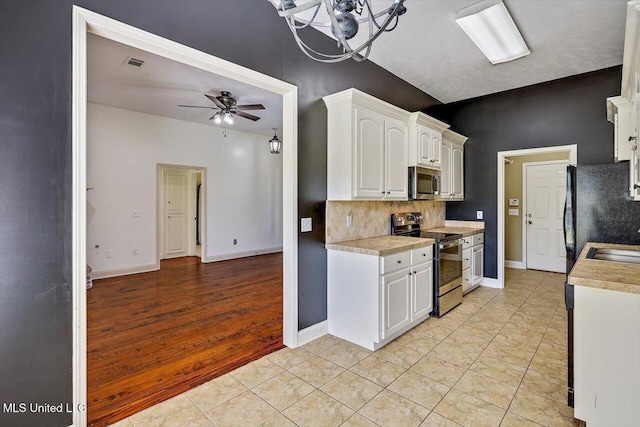kitchen featuring decorative backsplash, appliances with stainless steel finishes, light countertops, white cabinets, and ceiling fan with notable chandelier