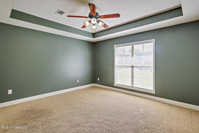spare room featuring ceiling fan, visible vents, baseboards, a raised ceiling, and carpet