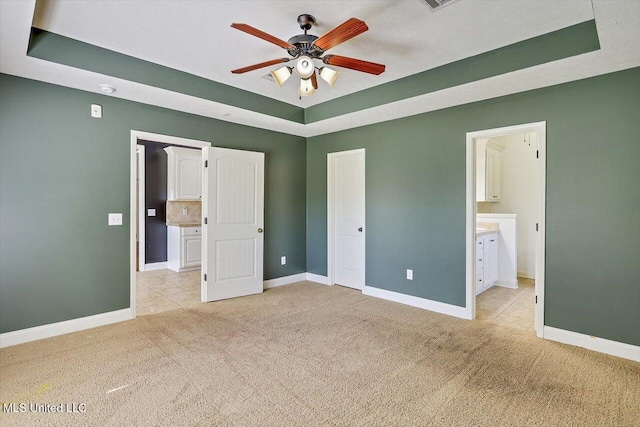 unfurnished bedroom featuring baseboards, a raised ceiling, ensuite bath, and light carpet
