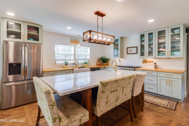 kitchen with stainless steel refrigerator with ice dispenser, a breakfast bar area, recessed lighting, a sink, and glass insert cabinets
