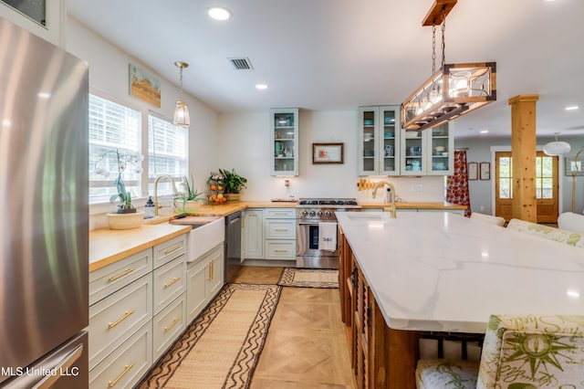 kitchen featuring appliances with stainless steel finishes, a sink, recessed lighting, light stone countertops, and glass insert cabinets