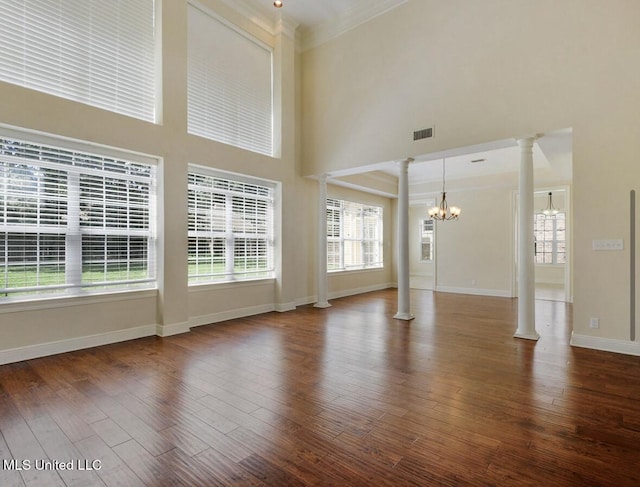 unfurnished living room featuring an inviting chandelier, wood-type flooring, a high ceiling, and ornate columns