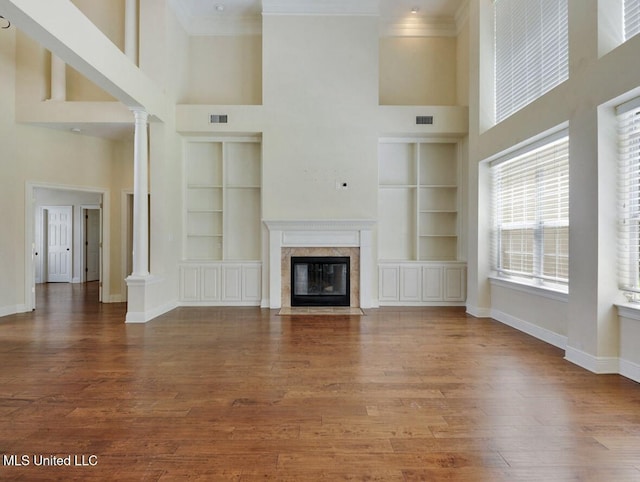 unfurnished living room with decorative columns, crown molding, built in features, a premium fireplace, and hardwood / wood-style floors