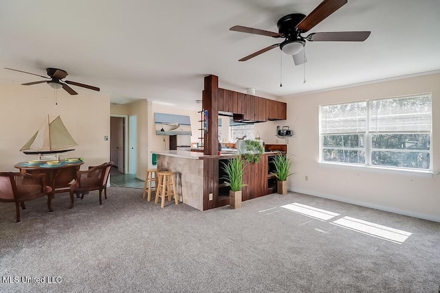 kitchen with ceiling fan, light colored carpet, a kitchen bar, and kitchen peninsula