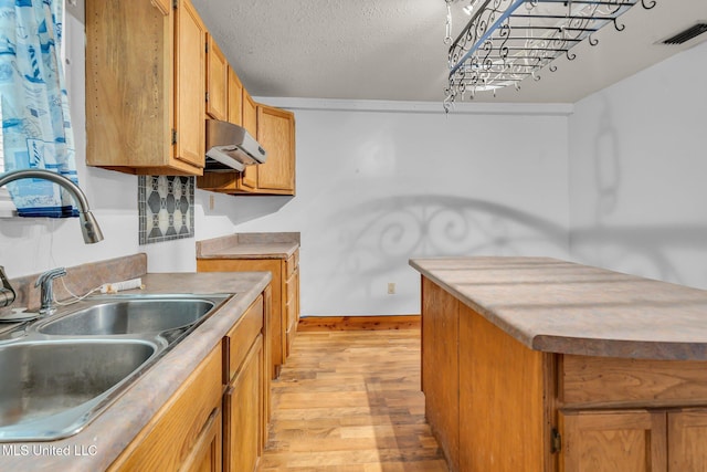 kitchen featuring a sink, light wood-type flooring, under cabinet range hood, brown cabinets, and baseboards
