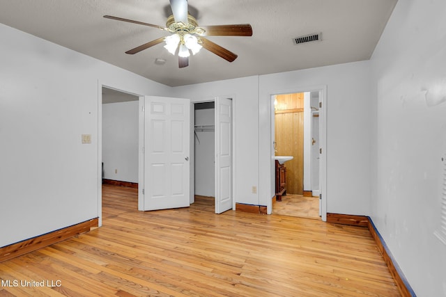 unfurnished bedroom featuring light wood-style floors, baseboards, a ceiling fan, ensuite bathroom, and a closet