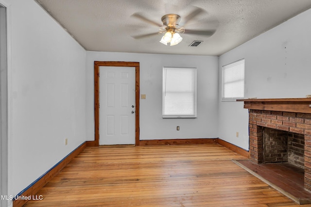 unfurnished living room with a textured ceiling, light wood finished floors, baseboards, ceiling fan, and a brick fireplace