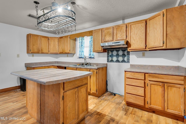 kitchen featuring a sink, under cabinet range hood, light wood-style flooring, a center island, and light countertops