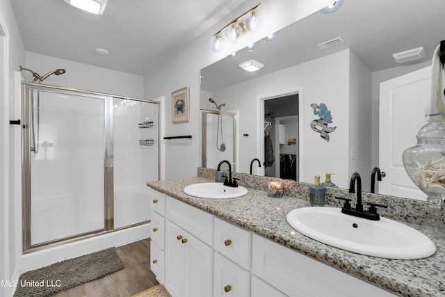 full bath featuring a shower stall, wood finished floors, double vanity, and a walk in closet