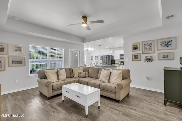 living room featuring a ceiling fan, a tray ceiling, wood finished floors, and recessed lighting