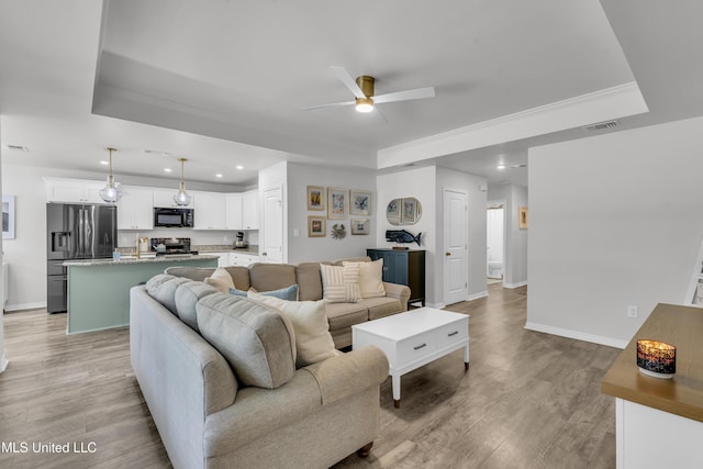 living area featuring a raised ceiling, a ceiling fan, recessed lighting, baseboards, and light wood-style flooring