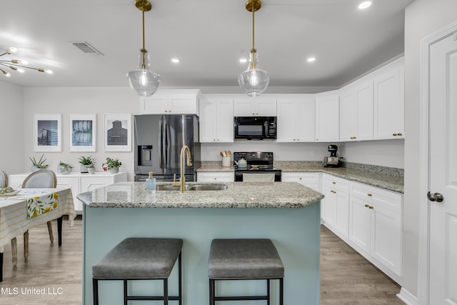 kitchen featuring black appliances, a sink, a kitchen island with sink, a kitchen bar, and white cabinets