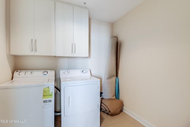 clothes washing area with cabinets, light tile patterned flooring, and washer and clothes dryer