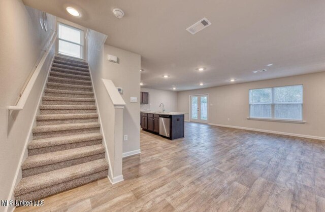 unfurnished living room with a sink, visible vents, light wood-type flooring, and baseboards