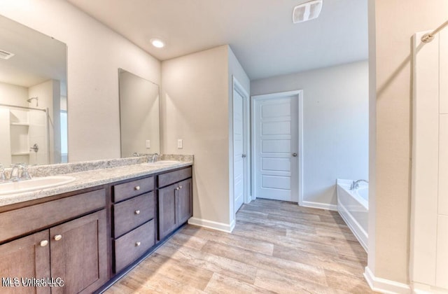 bathroom featuring a sink, wood finished floors, double vanity, and a bath