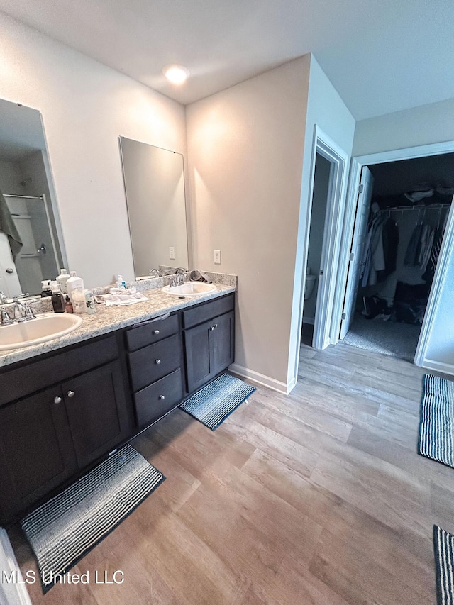 full bathroom featuring a sink, baseboards, wood finished floors, and double vanity