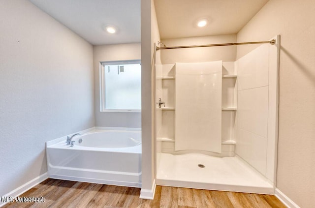 bathroom featuring a bath, baseboards, walk in shower, and wood finished floors