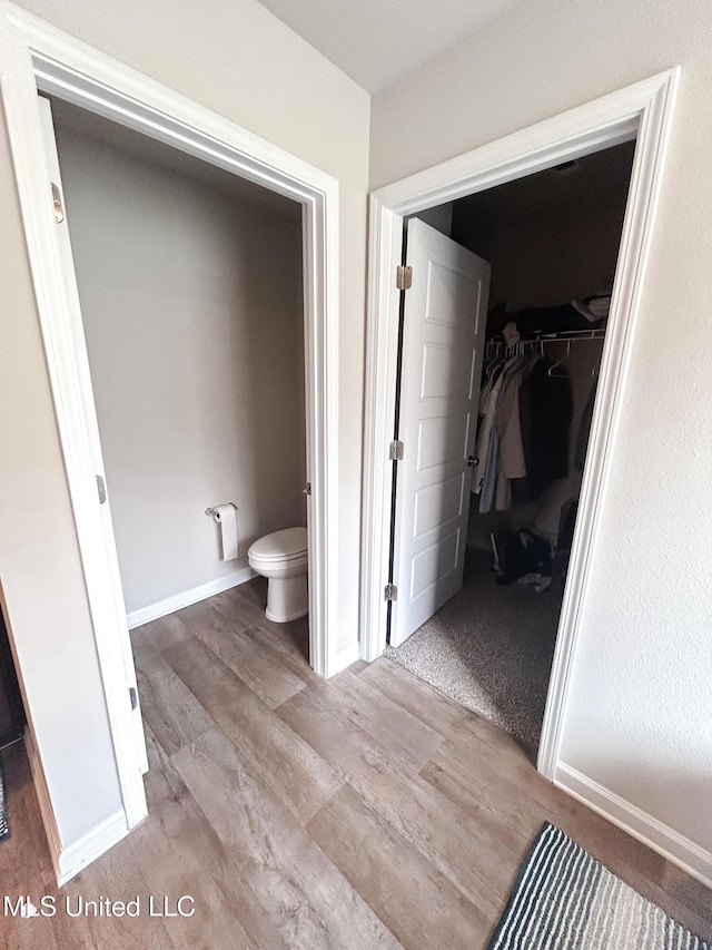 bathroom featuring toilet, a walk in closet, baseboards, and wood finished floors