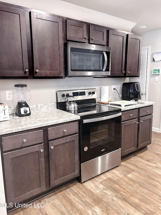 kitchen with light wood finished floors, dark brown cabinetry, appliances with stainless steel finishes, and light countertops