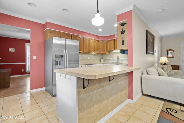 kitchen with light tile patterned floors, a peninsula, light countertops, stainless steel fridge, and crown molding