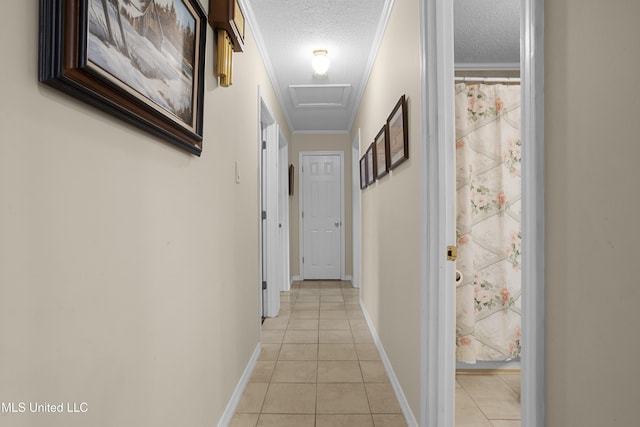 hallway with attic access, light tile patterned flooring, ornamental molding, and a textured ceiling