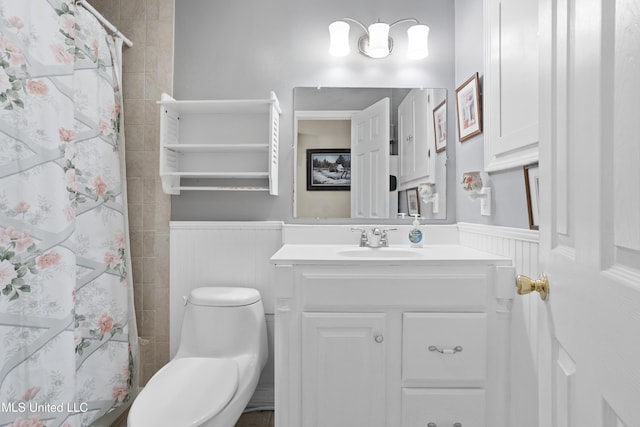 full bathroom featuring wainscoting, a tile shower, vanity, and toilet