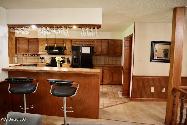 2440 E Church Rd, Southaven, MS 38671 - kitchen with black appliances, tile countertops, brown cabinets, a breakfast bar, and a wainscoted wall