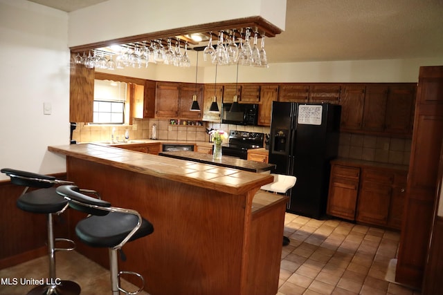 2440 E Church Rd, Southaven, MS 38671 - kitchen with tile countertops, black appliances, a breakfast bar area, and decorative backsplash
