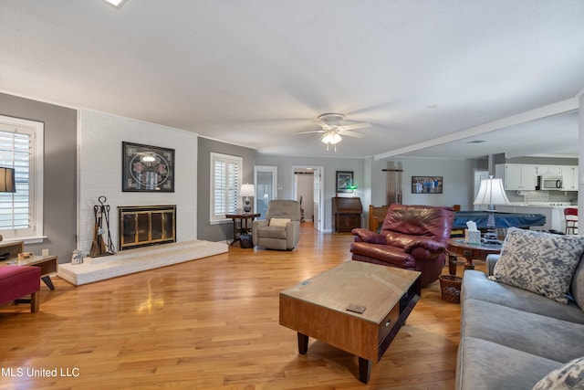 living room featuring plenty of natural light, a fireplace, light wood-type flooring, and ceiling fan