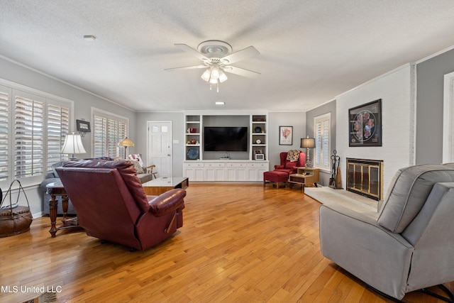 living room featuring crown molding, a brick fireplace, a textured ceiling, light hardwood / wood-style floors, and ceiling fan