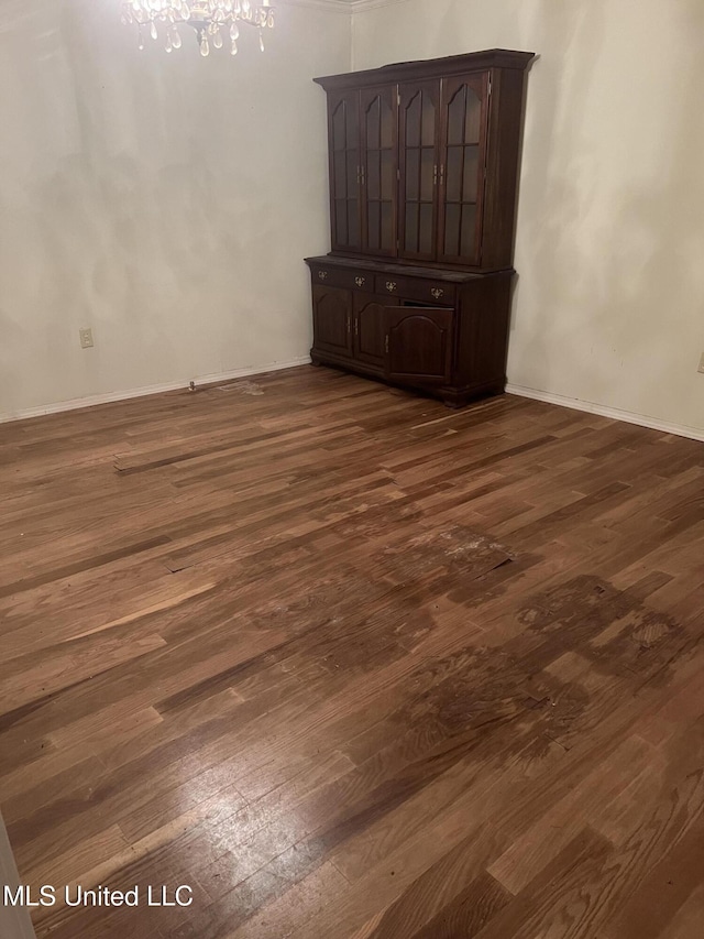 empty room with dark wood-style floors, a chandelier, and baseboards