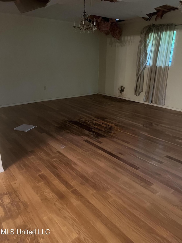 spare room featuring wood finished floors, a chandelier, and baseboards