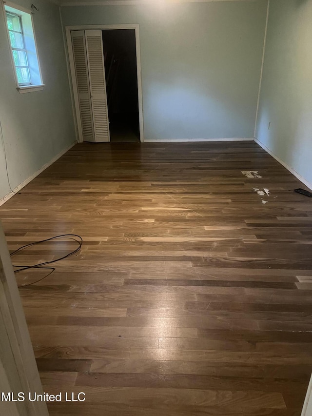 unfurnished bedroom featuring wood finished floors, a closet, and baseboards