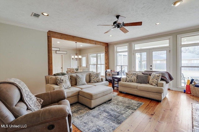 living area featuring visible vents, light wood-style flooring, ornamental molding, a textured ceiling, and french doors