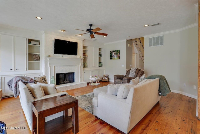 living area with visible vents, a fireplace, ornamental molding, light wood-style floors, and a textured ceiling