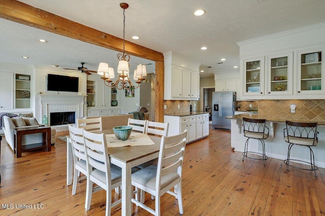 dining area with beamed ceiling, a fireplace, light wood-style floors, and ornamental molding