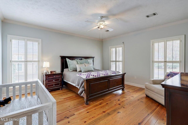 bedroom featuring baseboards, visible vents, a textured ceiling, crown molding, and light wood-type flooring