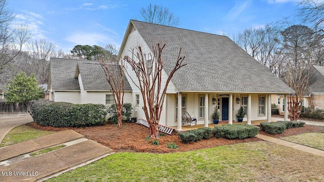 view of front facade featuring a porch, a front lawn, roof with shingles, and stucco siding