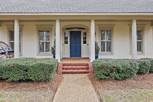 view of exterior entry with covered porch, stucco siding, and roof with shingles