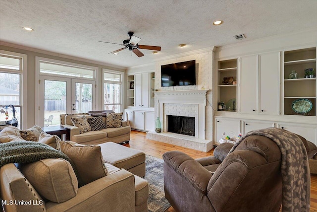 living room featuring wood finished floors, visible vents, french doors, a textured ceiling, and a brick fireplace