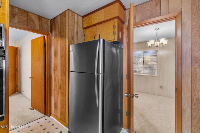 kitchen featuring stainless steel refrigerator, wooden walls, light colored carpet, a notable chandelier, and decorative light fixtures