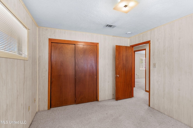 unfurnished bedroom featuring ornamental molding, a textured ceiling, light colored carpet, and a closet