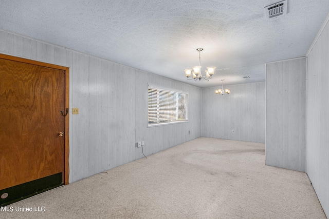 empty room featuring light carpet, an inviting chandelier, and a textured ceiling