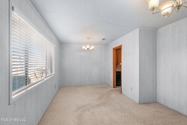 spare room featuring light carpet and a notable chandelier