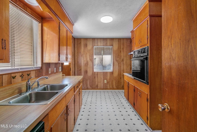 kitchen with a textured ceiling, oven, sink, and wooden walls