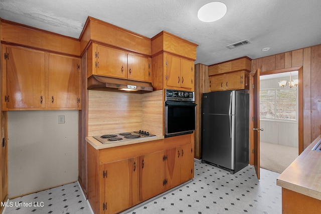 kitchen featuring wood walls, a textured ceiling, a chandelier, and stainless steel appliances