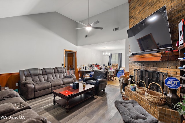 living room featuring ceiling fan with notable chandelier, a fireplace, wood-type flooring, and high vaulted ceiling