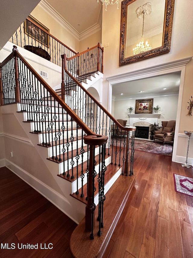 stairway featuring a notable chandelier, ornamental molding, wood-type flooring, and a high ceiling