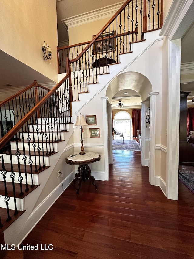 stairs with hardwood / wood-style flooring, ornamental molding, ceiling fan, and a towering ceiling