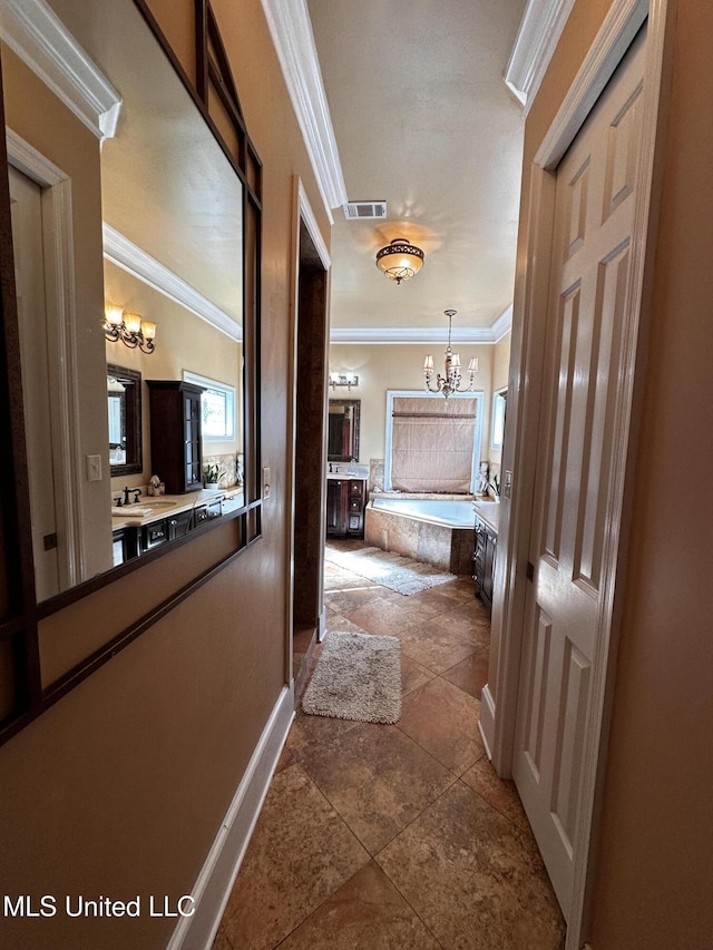 hall with dark tile patterned flooring, ornamental molding, and a chandelier